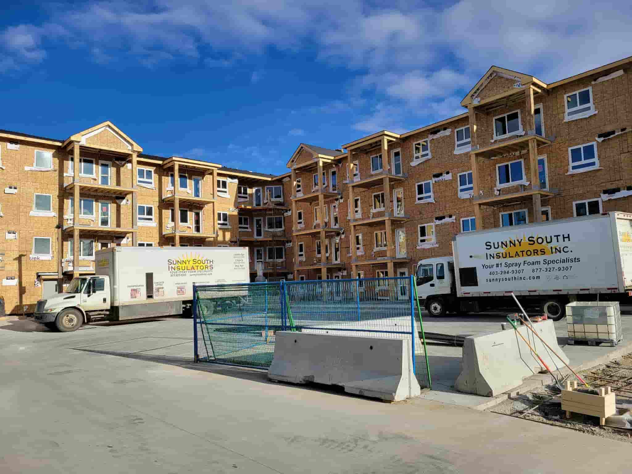 Construction site with insulation trucks parked in front of an unfinished building in Calgary, AB